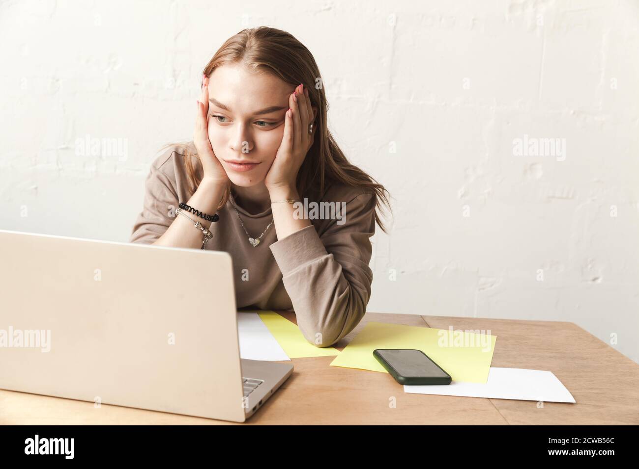 Müde blonde Mädchen Schüler ist in einem Klassenzimmer mit Laptop und Papiertücher auf einem Holzschreibtisch Stockfoto