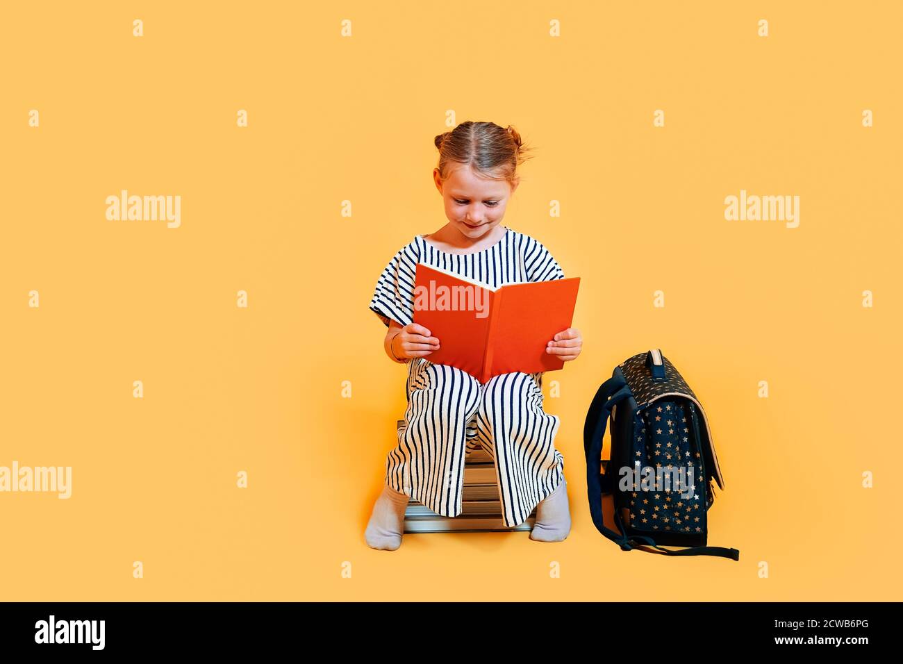 Ein sitzendes Schulmädchen lächelt und liest ein Buch. Lernkonzept in der Schule. Stockfoto