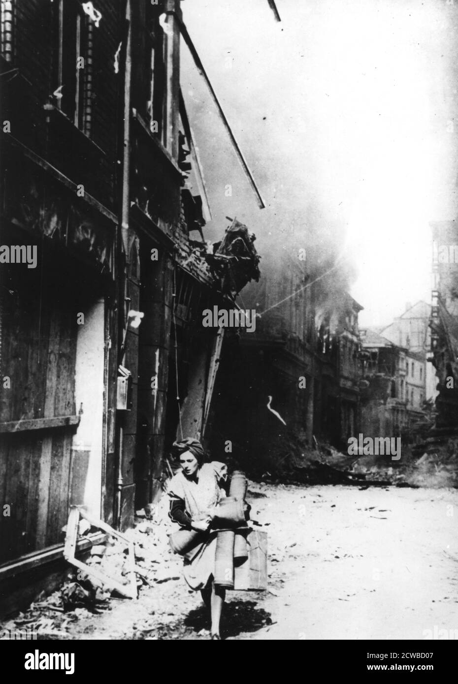 Eine Frau, die ihr brennendes Haus mit ein paar Habseligkeiten in einer bombardierten Straße verlässt, Deutschland, 1945. Der Fotograf ist unbekannt. Stockfoto