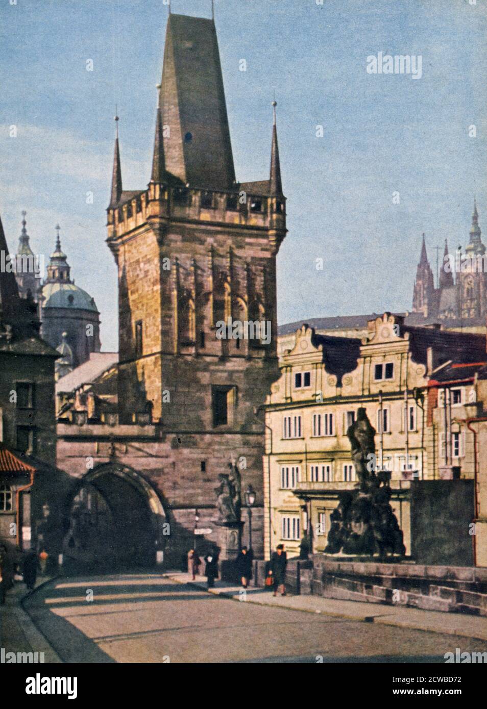 Die Altstadt Ende der König-Charles-Brücke, Prag, Tschechische Republik, 1943. Der Bau der Brücke über die Moldau begann 1357 unter der Herrschaft von Karl IV., König von Böhmen und Kaiser des Heiligen Römischen Reiches. Die Brücke ist aus Stein gebaut, 516 Meter lang, und hat 16 Bögen mit Eiswächtern geschützt. Die Brücke wird von zwei Reihen von 15 Statuen flankiert. Ein Druck aus Signal, Februar 1943. Signal war eine Zeitschrift des Deutschen Dritten Reiches von 1940 bis 1945. Der Künstler ist unbekannt. Stockfoto