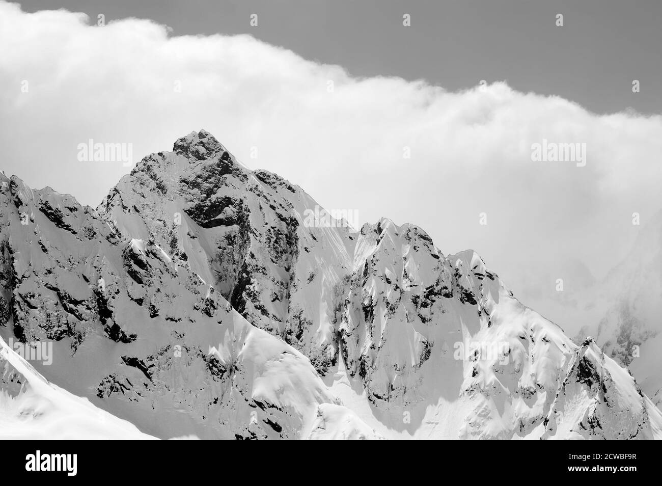 Schneebedeckte, sonnenbeschienenen Winterberge in Wolken. Kaukasus-Gebirge, Region Dombay. Blick von der Skipiste. Schwarz-weiß getönte Landschaft. Stockfoto