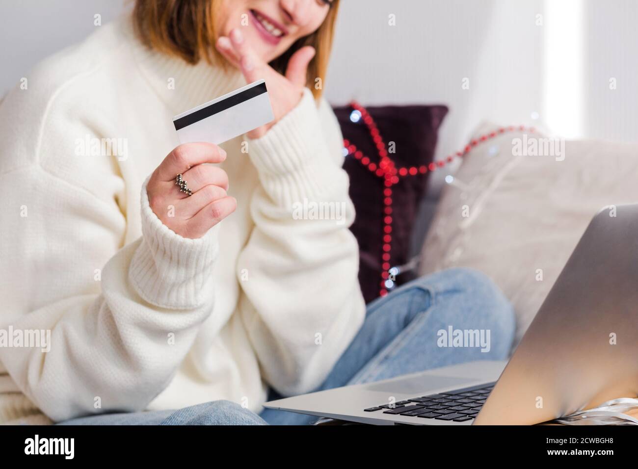 Eine junge Frau in einem weißen Pullover, macht Weihnachtsmann Hut Online-Einkäufe mit einem Notebook und einer Kreditkarte. Neujahr Shopping und weihnachtsverkauf Stockfoto