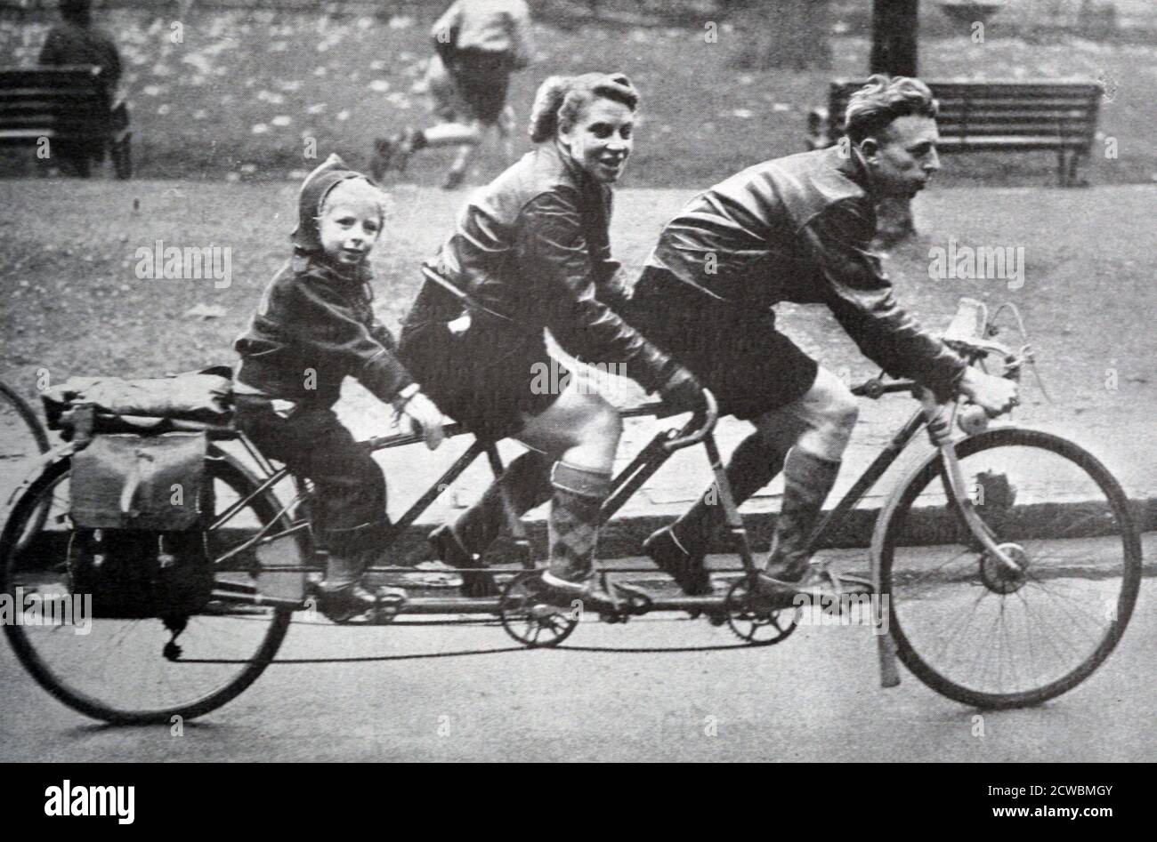 Schwarz-Weiß-Foto einer Familie, die auf einem Fahrrad für drei Personen fährt, darunter ein Vater, seine junge Frau und ihr Kind. Stockfoto