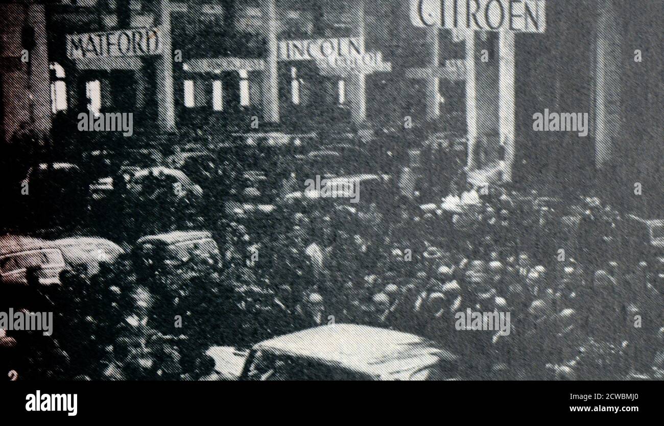 Schwarz-Weiß-Foto über die Leistungen in der Automobilherstellung im Jahr 1938; ein Auto Showroom mit Menschen gefüllt und mit Fahnen verschiedener Marken hängen von der Decke. Stockfoto