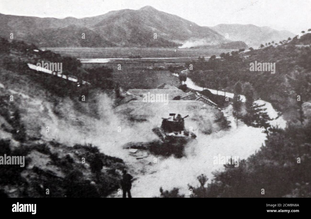 Schwarz-Weiß-Fotografie des Koreakrieges (1950-1953); amerikanische Infanteristen, die unter dem Schutz eines Panzers vorrücken, der das Feuer auf ein vom Feind besetztes Dorf eröffnet. Stockfoto