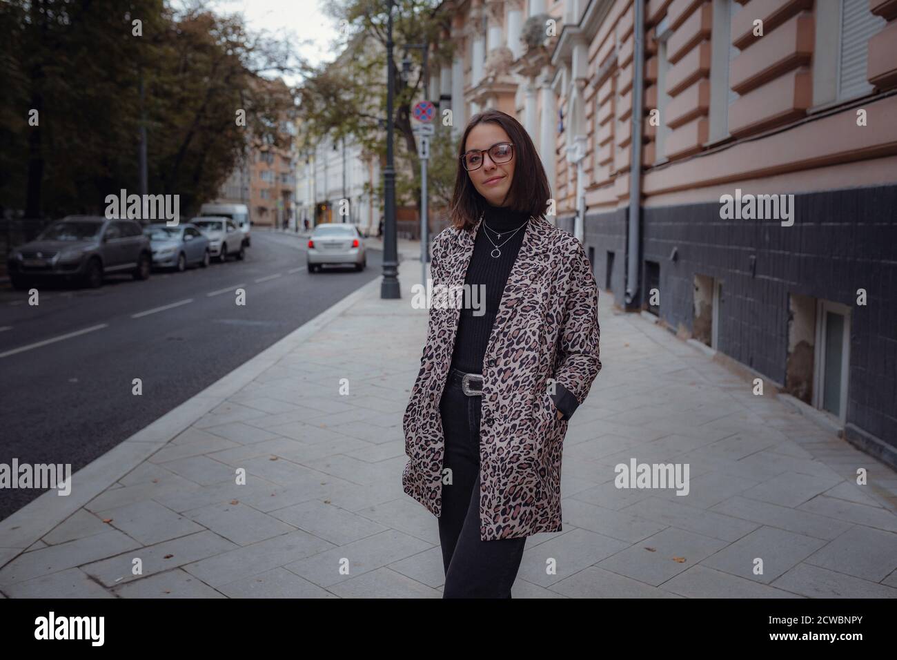 Schöne junge Brünette Frau geht in Moskau. In einer trendigen Leopardenjacke. Lächelnd und spazierend auf der Stadt. Einkaufen gehen. Stockfoto