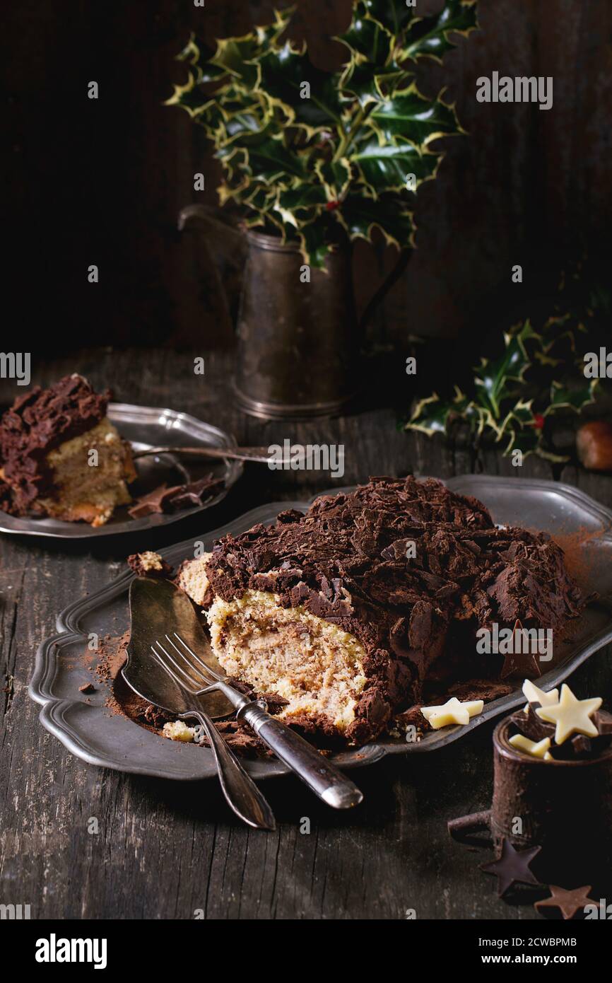 Geschnittene hausgemachte Weihnachtsschokolade yule Log mit Kastaniencreme auf Vintage-Teller mit Gabeln, Schokoladensternen und Stechpalme über alten Holztisch Stockfoto