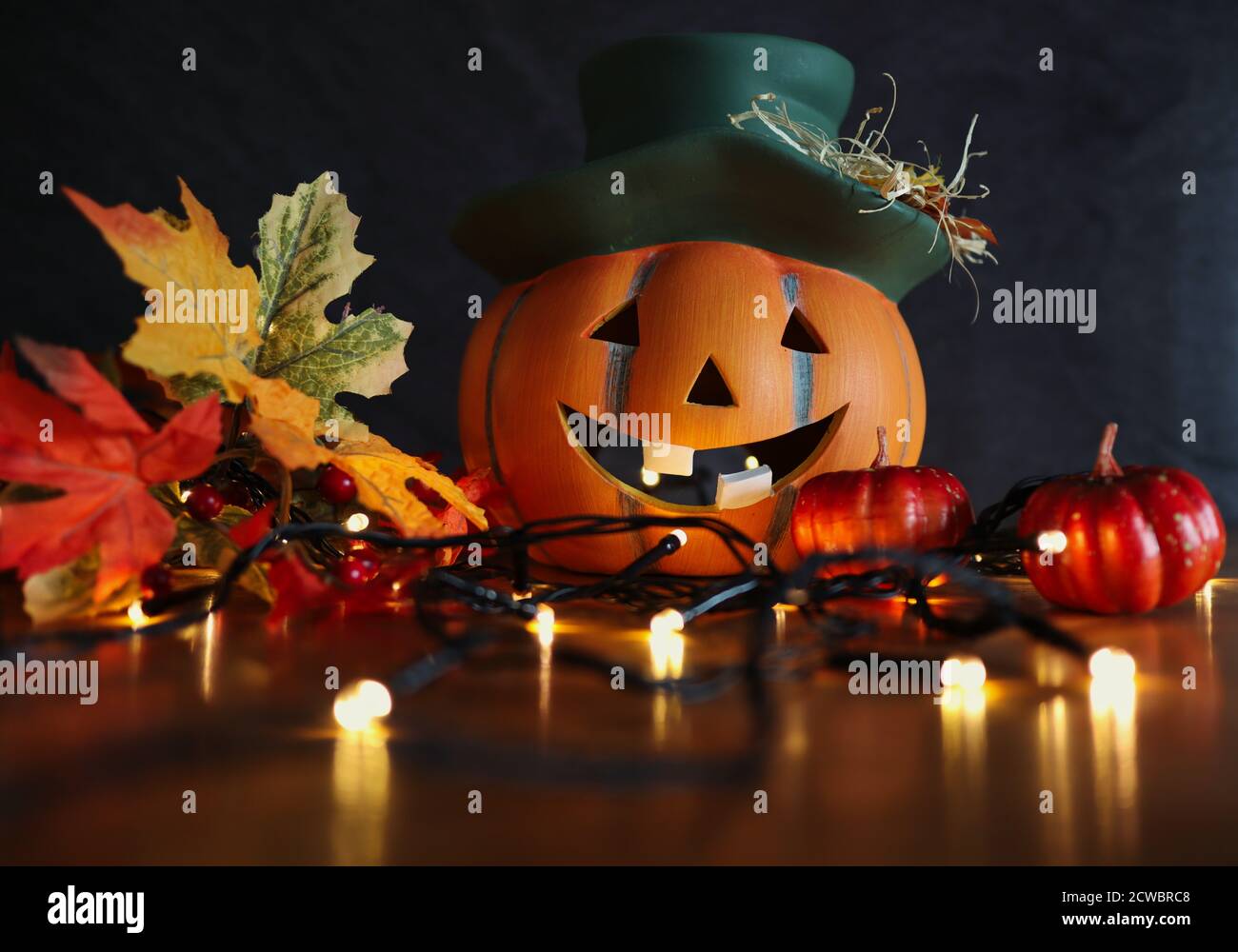 Keramik Halloween Orange Kürbis mit Lächeln mit künstlichen Herbstblättern und blinkenden Lichtern. Herbst und Halloween Vibes. Stockfoto