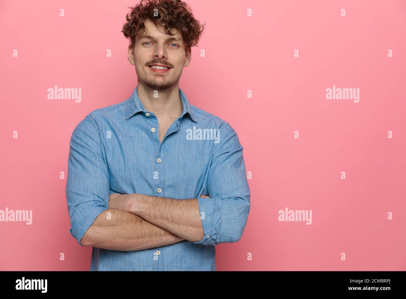 Glücklicher junger Kerl lächelnd und die Arme kreuzend, stehend auf rosafarbenem Hintergrund Stockfoto