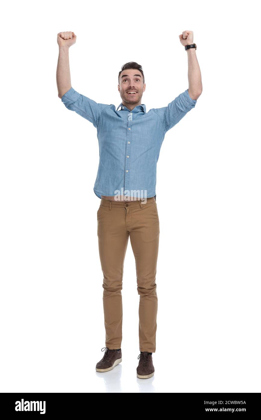 Hoffnungsvoller Casual Mann hält beide Fäuste in der Luft und lächelt, während das blaue Hemd trägt, auf weißem Studio Hintergrund stehend Stockfoto