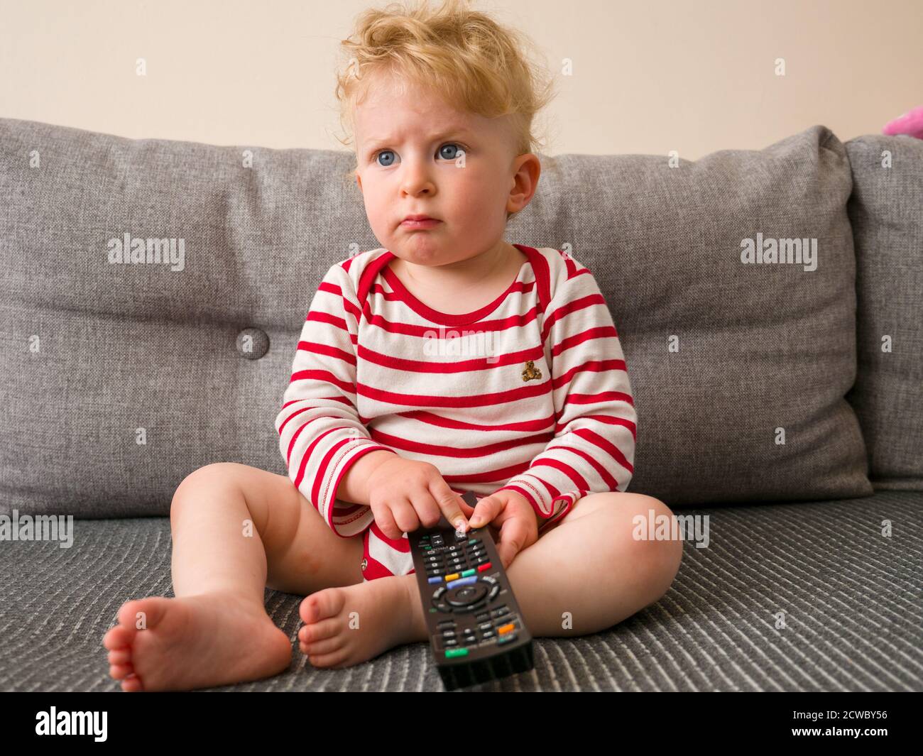 Ein Jahr altes Baby mit Fernbedienung zum Fernsehen Stockfoto