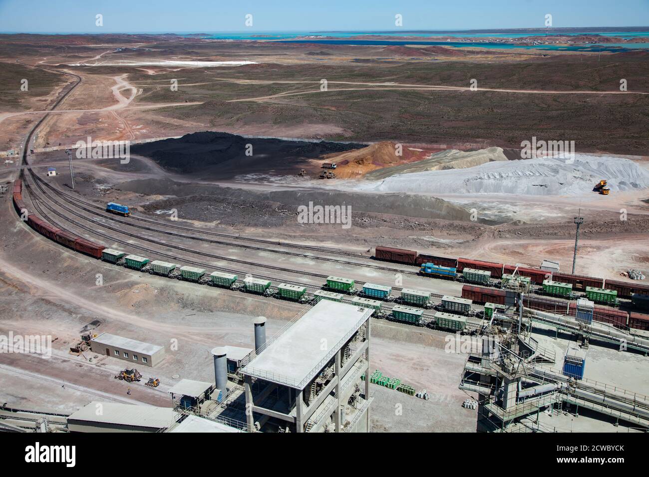 Mynaral/Kasachstan, Zementwerk von Jambyl. Cargo-Zug-Terminal und Haufen von Klinker Mineralien. Balkhash See am Horizont. Stockfoto