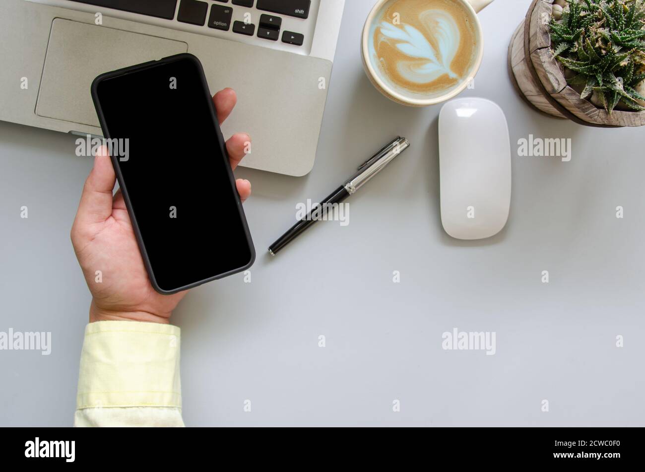 Männliche Hand hält Smartphone, Computer, Stift, Kaffee, Maus auf Schreibtisch Tisch mit Kopieplatz Stockfoto