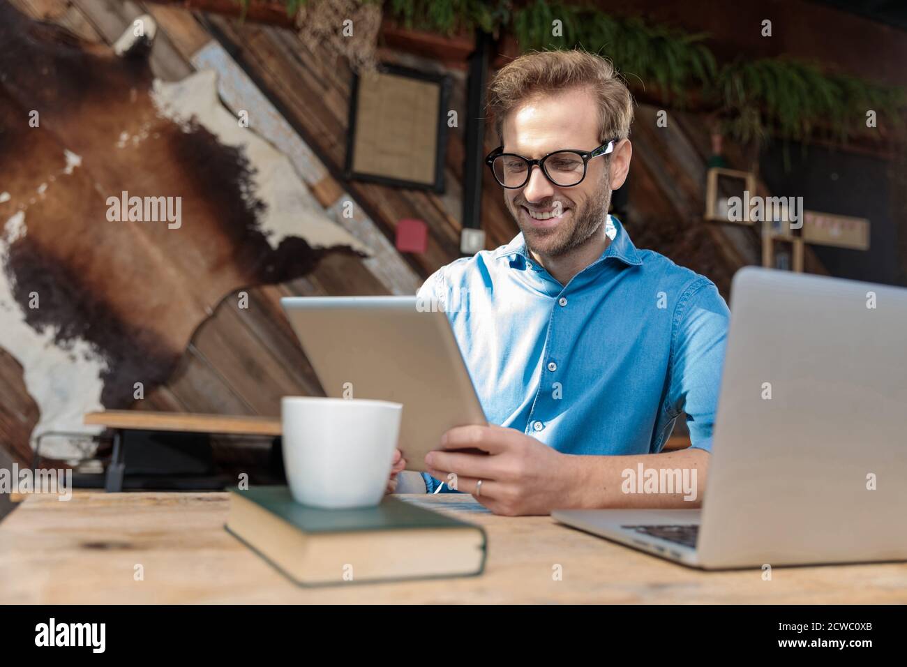 Ein Geschäftsmann mit Brille sitzt am Schreibtisch und arbeitet an ihm Die Tablette im Coffeeshop war gut Stockfoto