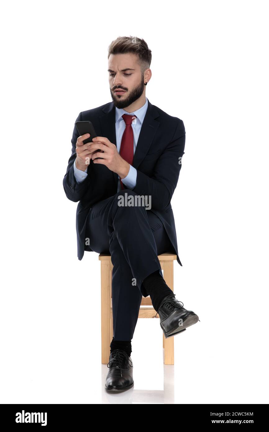 Besorgt jungen Geschäftsmann E-Mails und SMS-Nachrichten auf Handy, sitzen isoliert auf weißem Hintergrund Stockfoto