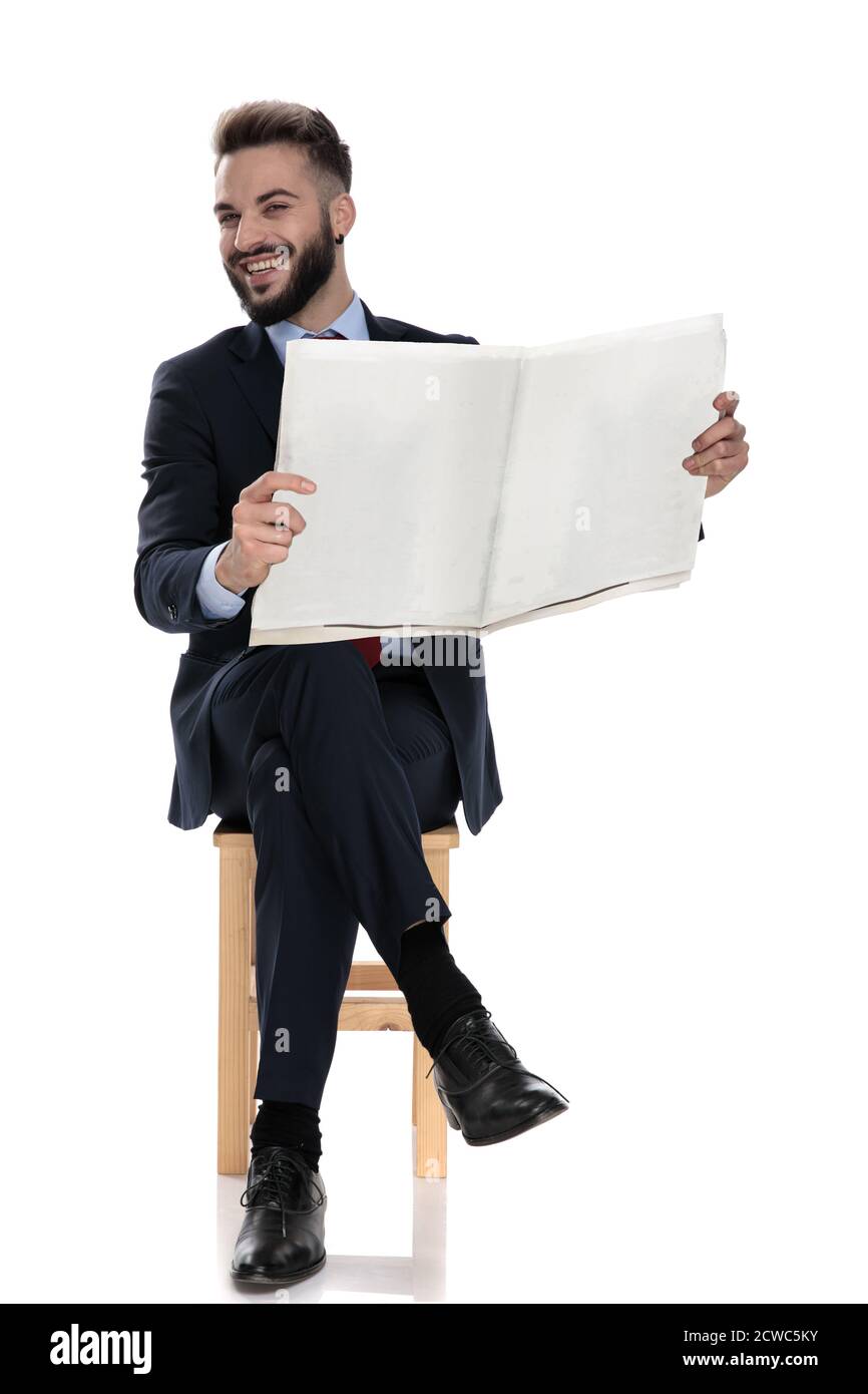 Glücklicher junger Geschäftsmann Zeitung lesen und lachen, sitzen isoliert auf weißem Hintergrund Stockfoto
