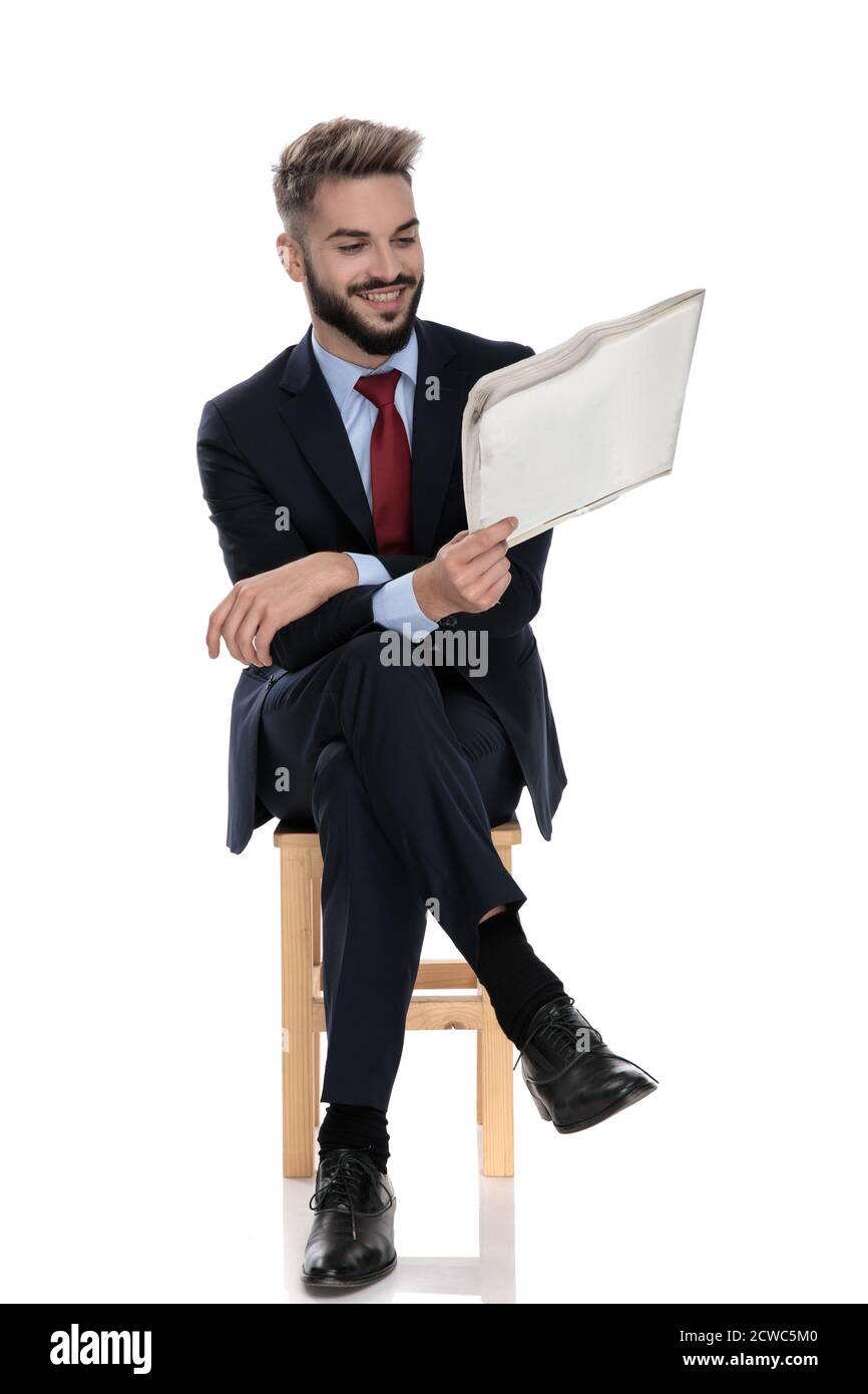 Glücklicher junger Geschäftsmann lächelnd und Zeitung lesen, sitzen isoliert auf weißem Hintergrund Stockfoto