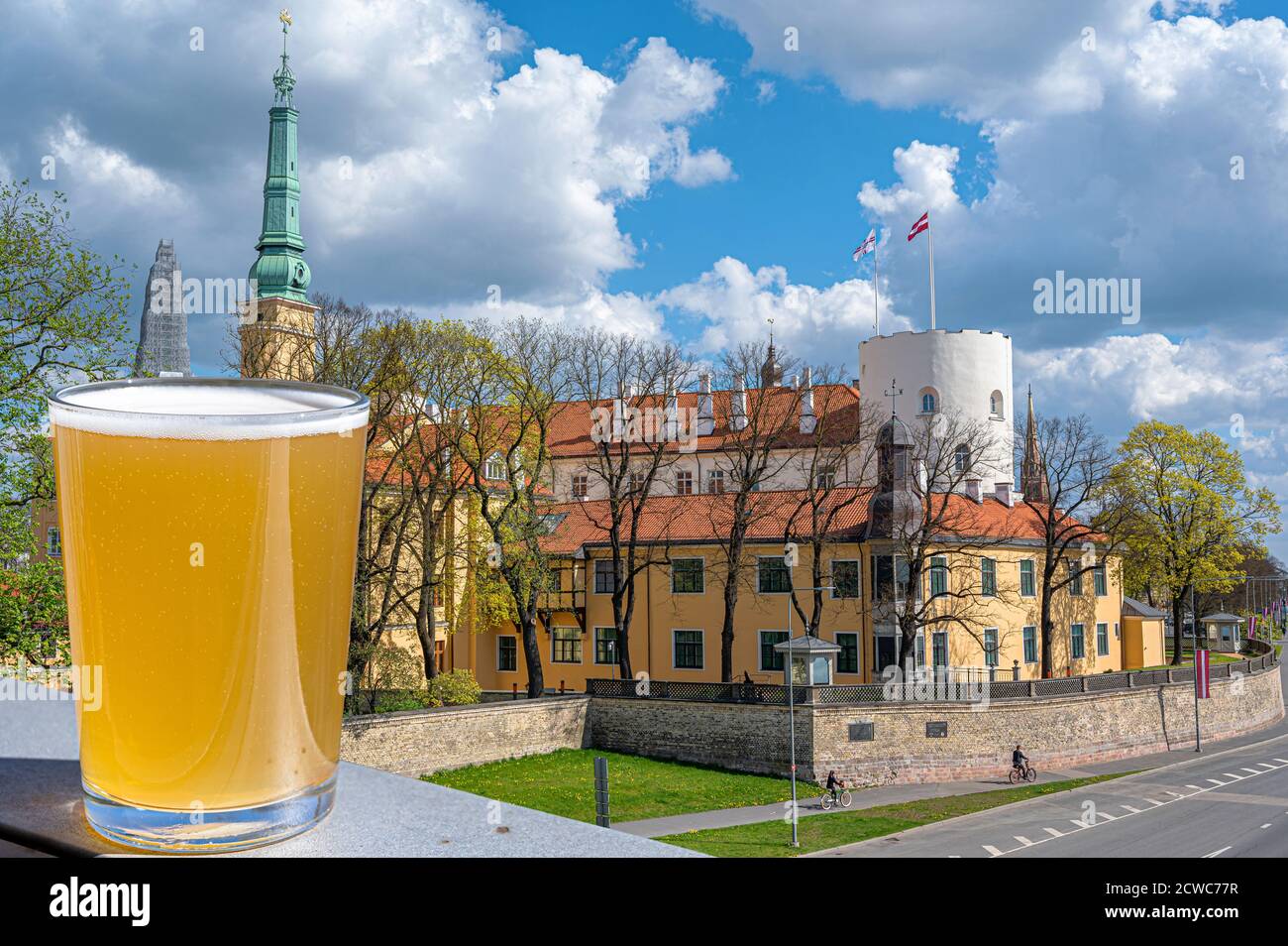 Ein Glas leichtes Bier mit Blick auf die Burg von Riga während eines sonnigen Tages in Riga, Lettland. Die Rigaer Burg ist eine Burg am Ufer des Flusses Daugava. Stockfoto