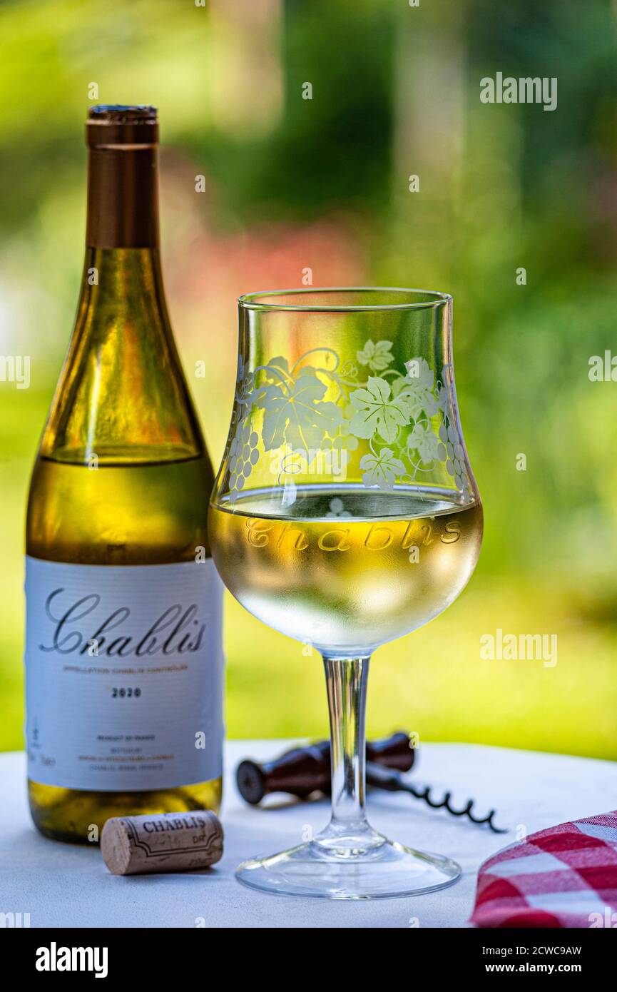 Chablis Flasche 2020 und Spezialität ‘Chablis’ gravierten Weinglas im Freien auf Gartenterrasse Tisch mit Kork & Korkenzieher in späten Nachmittag Sonne. Stockfoto