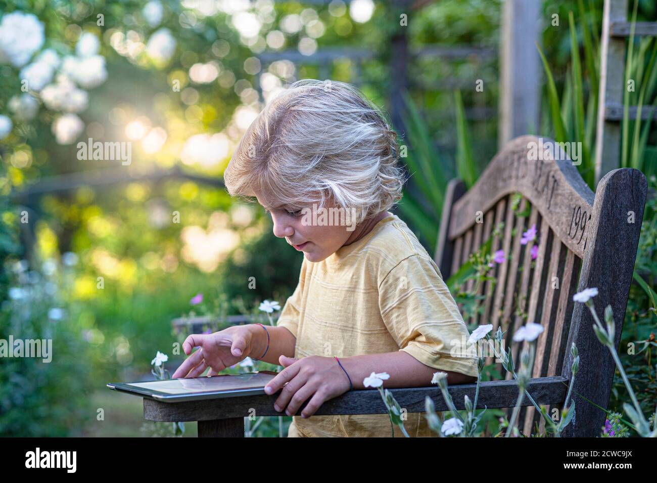 Kleinkind iPad Internet Sicherheit blonde junge 8-10 Jahre im floralen Garden glücklich mit seinem intelligenten Apple iPad Tablet-Computer im Freien In Blumengarten-Situation Stockfoto