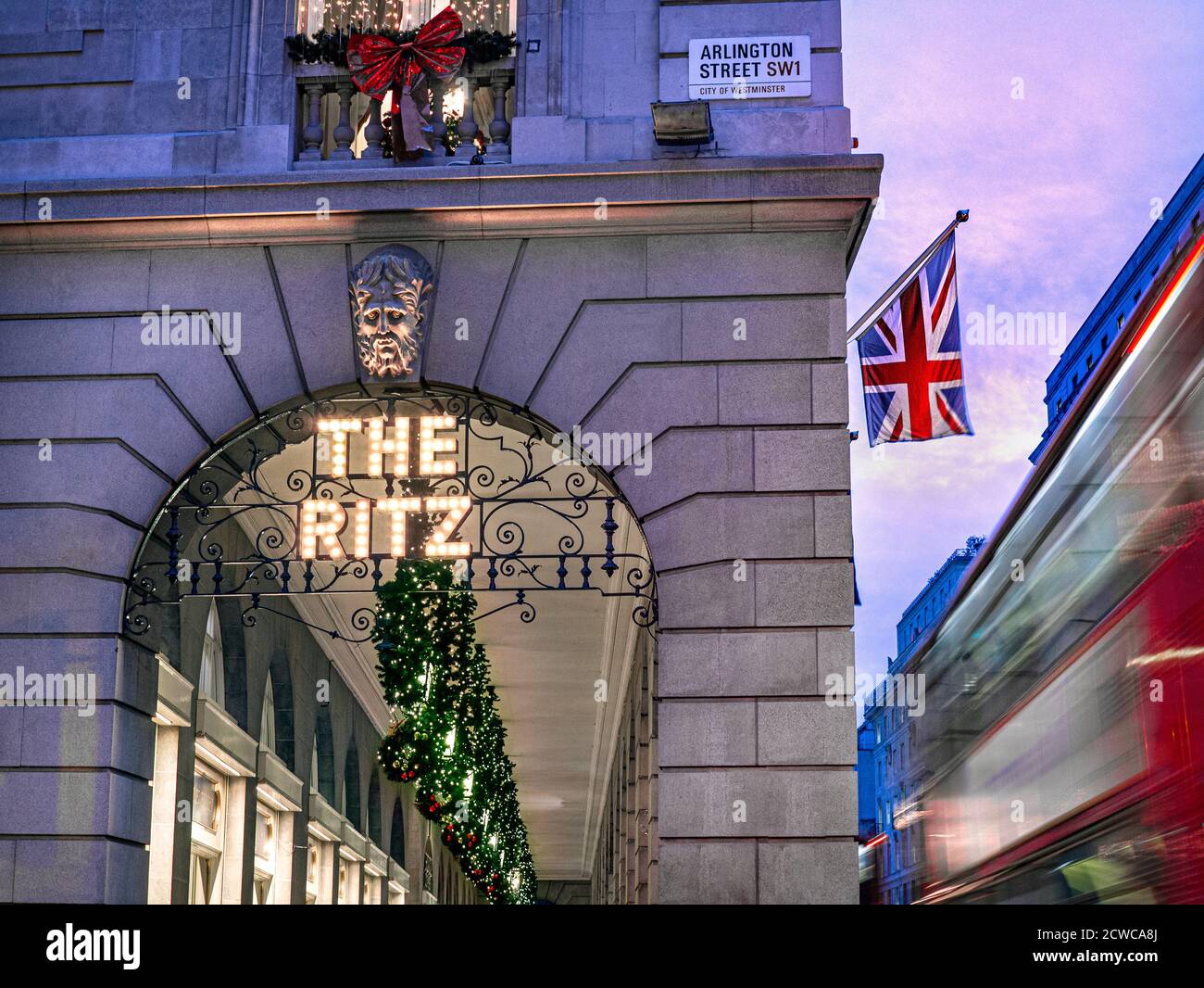 The Ritz Hotel zu Weihnachten, Abendlicht festliche Jahreszeit, Abendlicht ‘The Ritz’ Schild beleuchtet und eine Union Jack Flagge angezeigt, roten London Bus vorbei mit Geschwindigkeit Unschärfe. Arlington Street Piccadilly London, Großbritannien Stockfoto