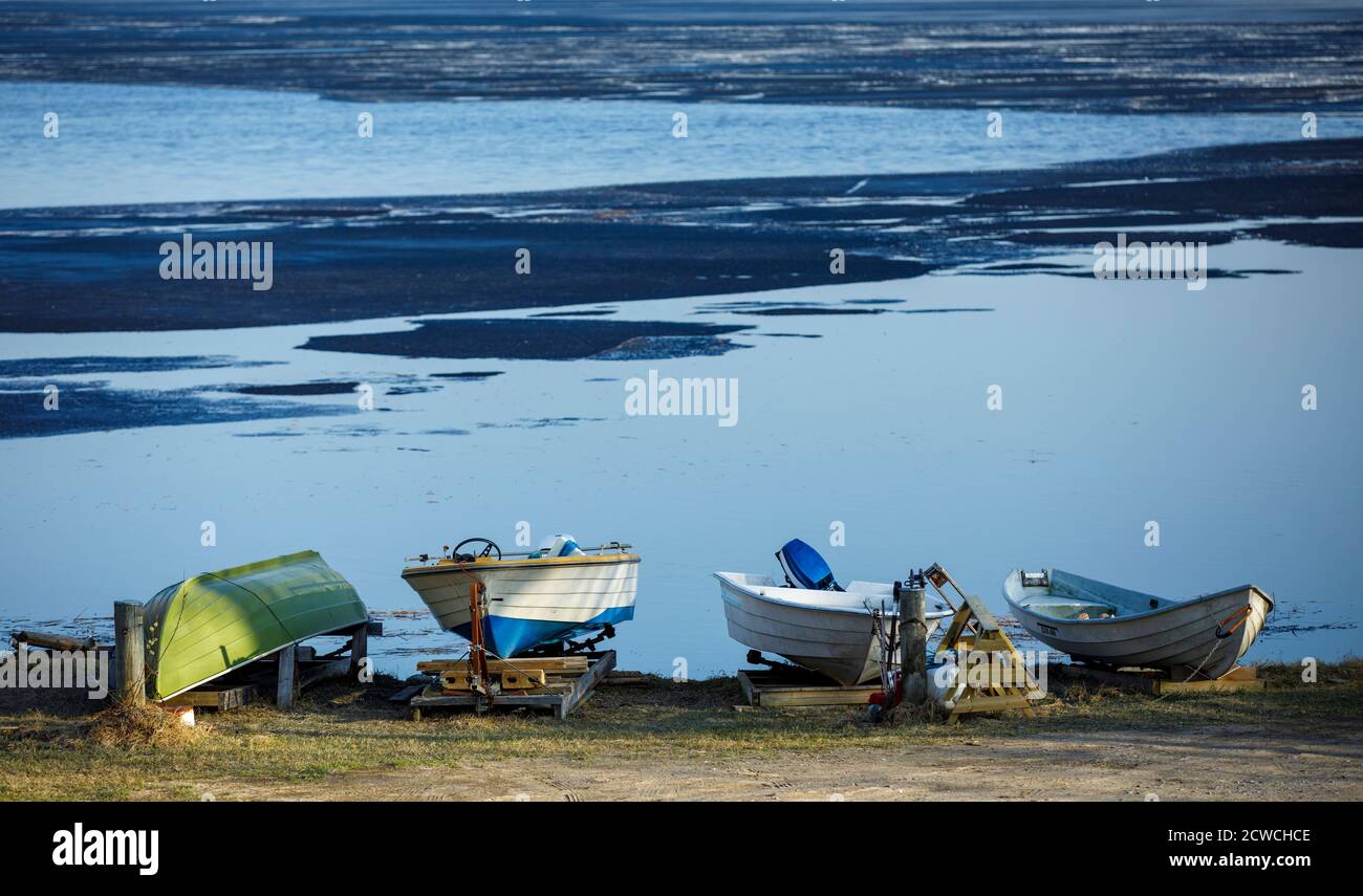 Kleine Ruderboote schaufeln Schlauchboote, die am Strand durch Schmelzsee in Spring, Finnland, gelagert werden Stockfoto