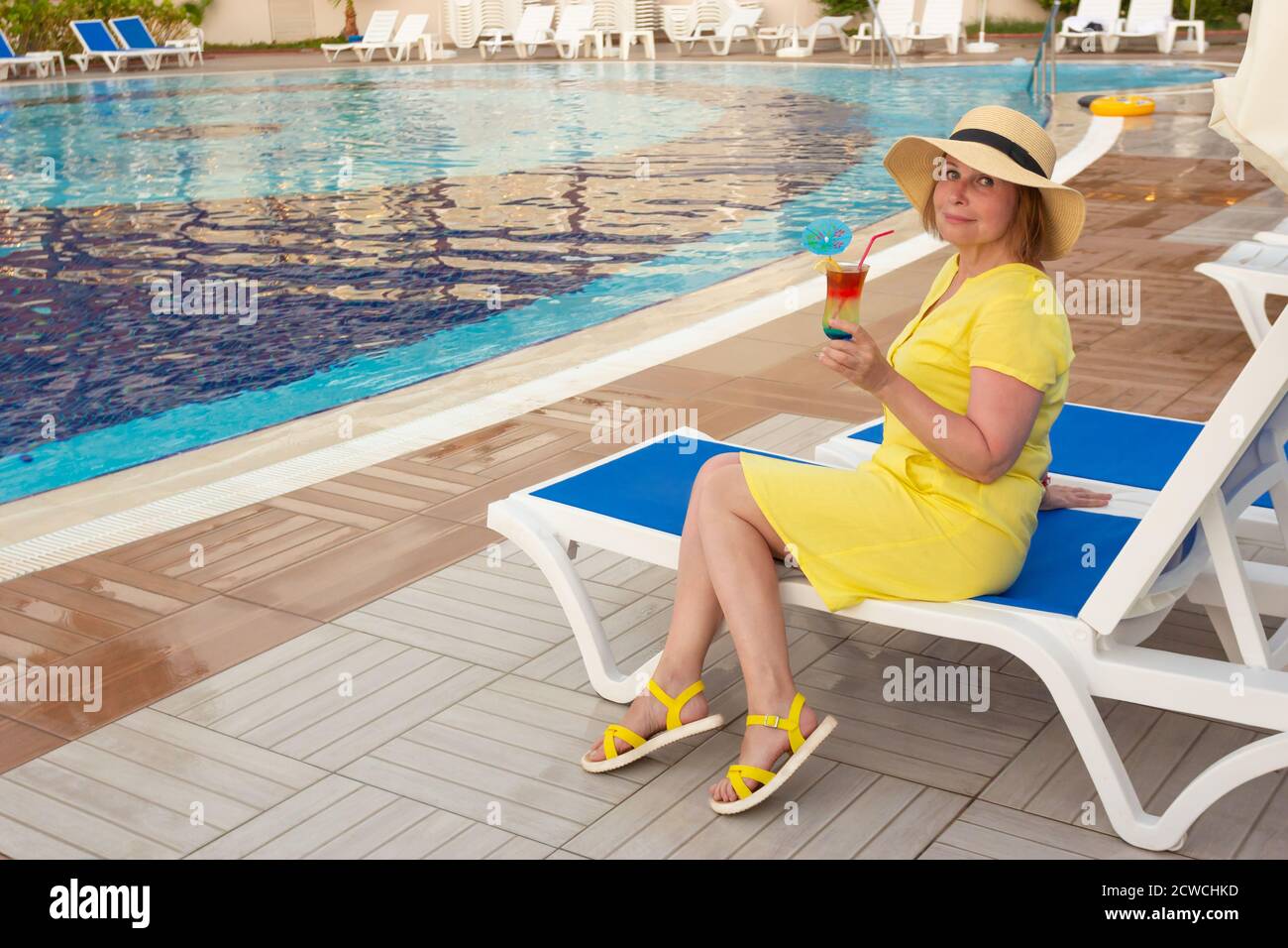 Glückliche reife Frau entspannt sich mit Cocktail auf der Sonnenliege am Pool des Resorts. Stockfoto