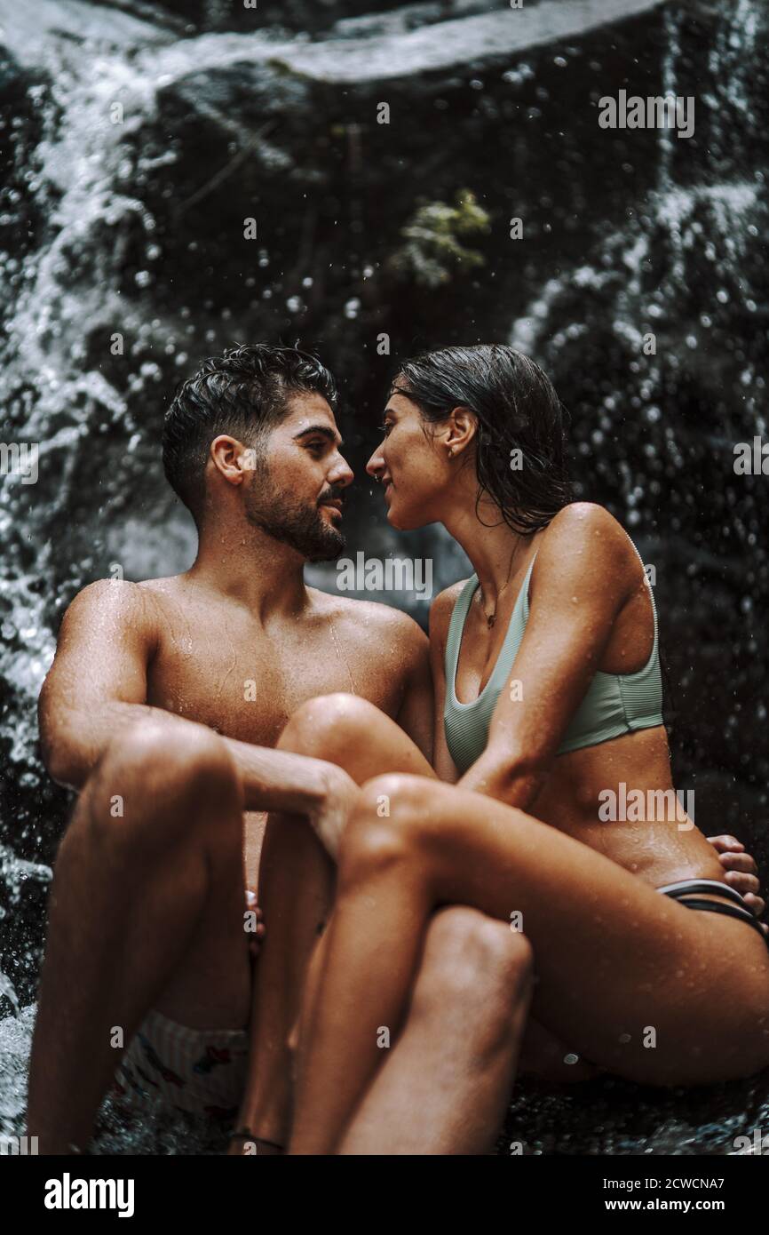 Nettes Paar sitzt auf einem Felsen und sind dabei Kuss unter dem Wasserfall Stockfoto