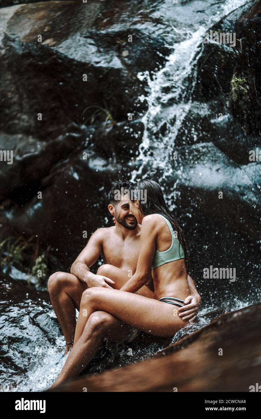 Nettes Paar sitzt auf einem Felsen und sind dabei Kuss unter dem Wasserfall Stockfoto