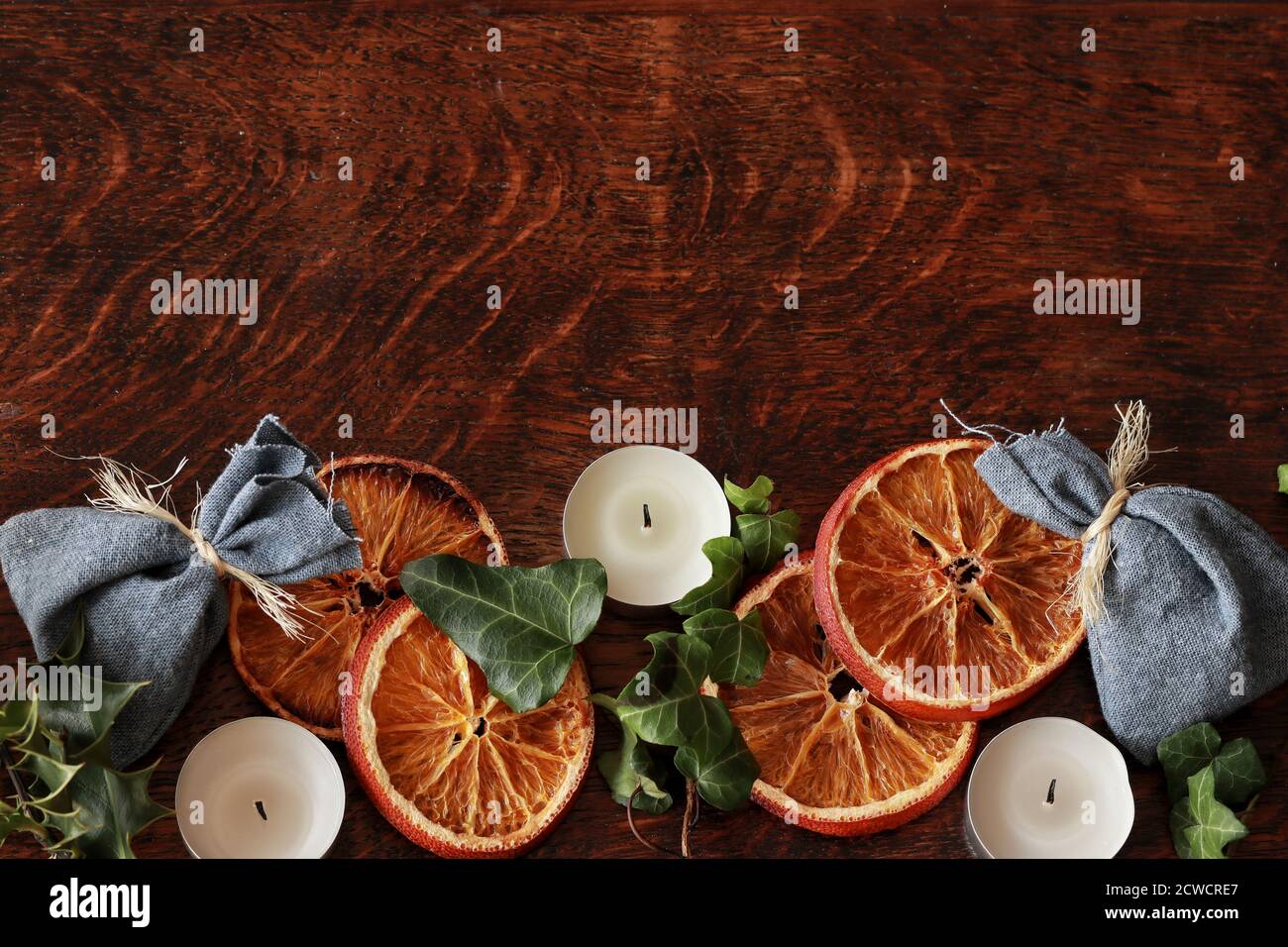 Dunkelbrauner Holztischhintergrund für Text, dekoriert mit getrocknetem Orange, Efeu Evergreens, blauen Baumwolltaschen, um festlich und gemütlich für Yule aussehen Stockfoto