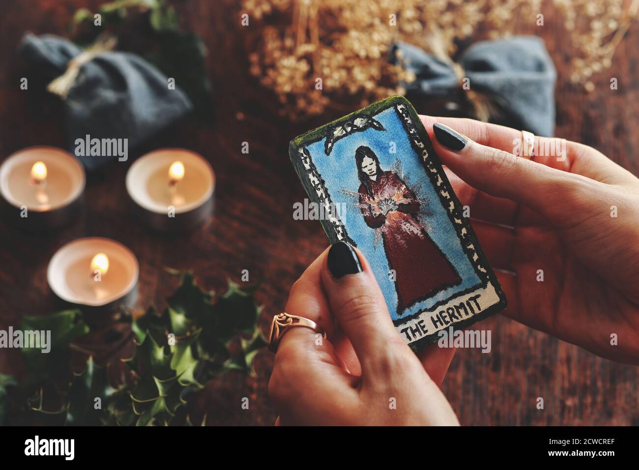 Wiccan Hexe hält eine kleine Hand bemalte (ermachte) Einsiedler Tarot-Karte in ihren Händen. Gemütliche warme Yule Winter Sonnenwende (Weihnachten) Hintergrund Stockfoto