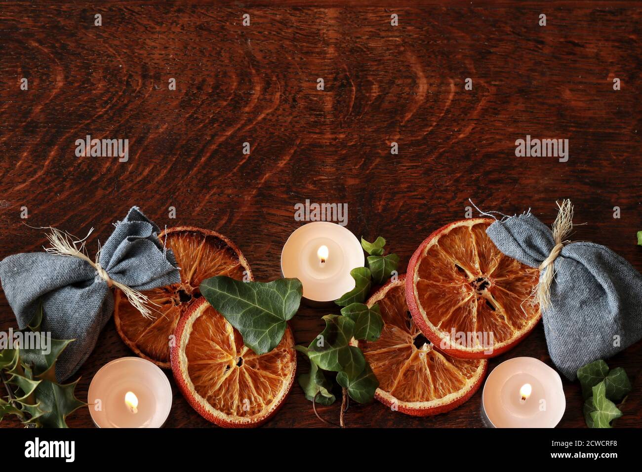 Dunkelbrauner Holztischhintergrund für Text, dekoriert mit getrocknetem Orange, Efeu Evergreens, blauen Baumwolltaschen, um festlich und gemütlich für Yule aussehen Stockfoto