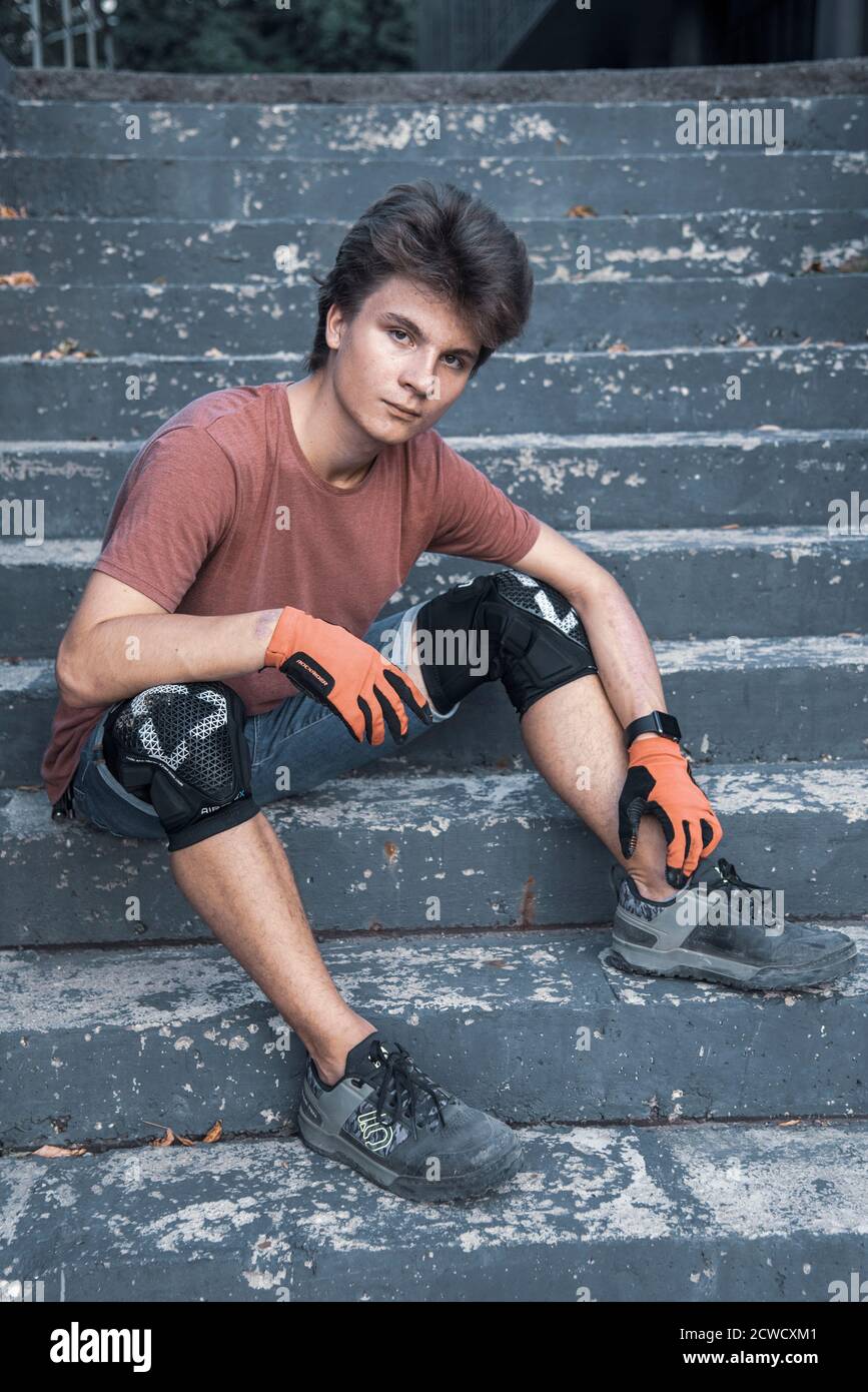 Ein Teenager trägt Knieschoner, Fahrradhandschuhe und Stiefel sitzt auf einem Schritt an einem warmen Sommertag. Stockfoto