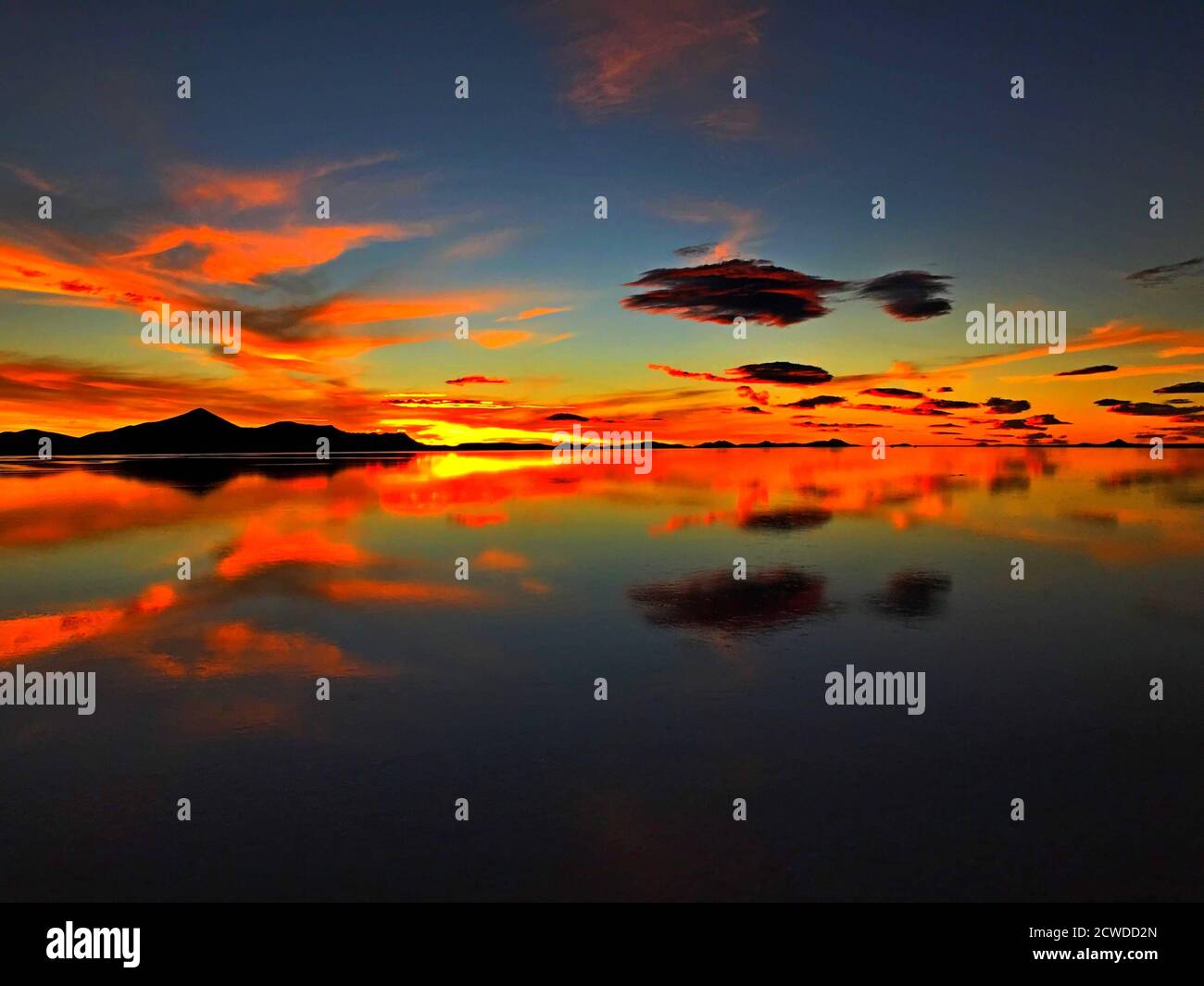 Beeindruckender orangefarbener Sonnenuntergang über dem Salzsee Uyuni. Atemberaubende Wolkenlandschaft. Magische Wolken spiegeln sich im Wasser. Schöne Nacht. Übernachtung in Bolivien. Stockfoto