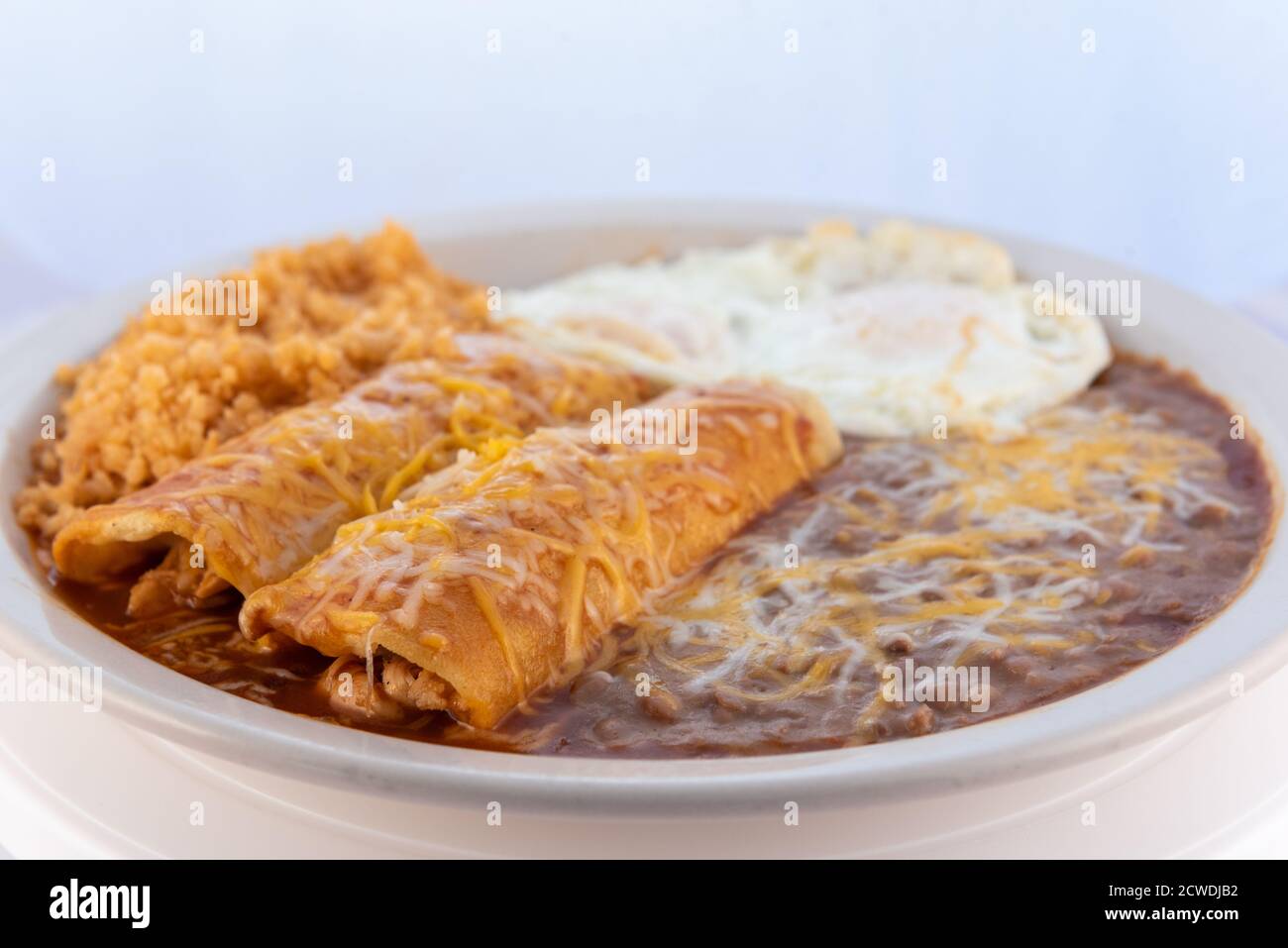 Großzügige Mahlzeit von einem herzhaften Paar Frühstück Enchiladas kombiniert mit gebratenen Bohnen, Reis und Eier. Stockfoto