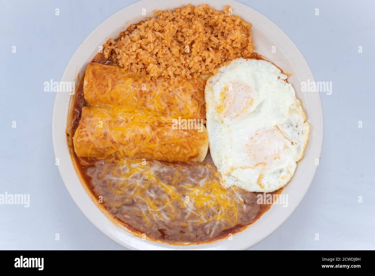 Blick von oben auf eine großzügige Mahlzeit von einem herzhaften Paar Frühstück Enchiladas kombiniert mit gebratenen Bohnen, Reis und Eiern. Stockfoto