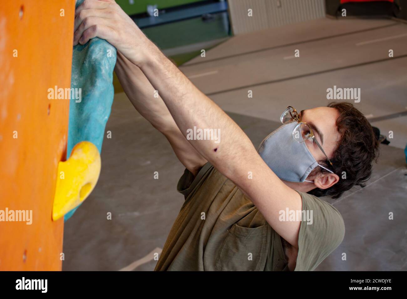 Nahaufnahme eines Mannes, der eine COVID-19 Pandemie trägt Mask klettert eine Boulderwand in einer Kletterhalle nach Richtlinien zur sozialen Distanz für Bewegung Stockfoto
