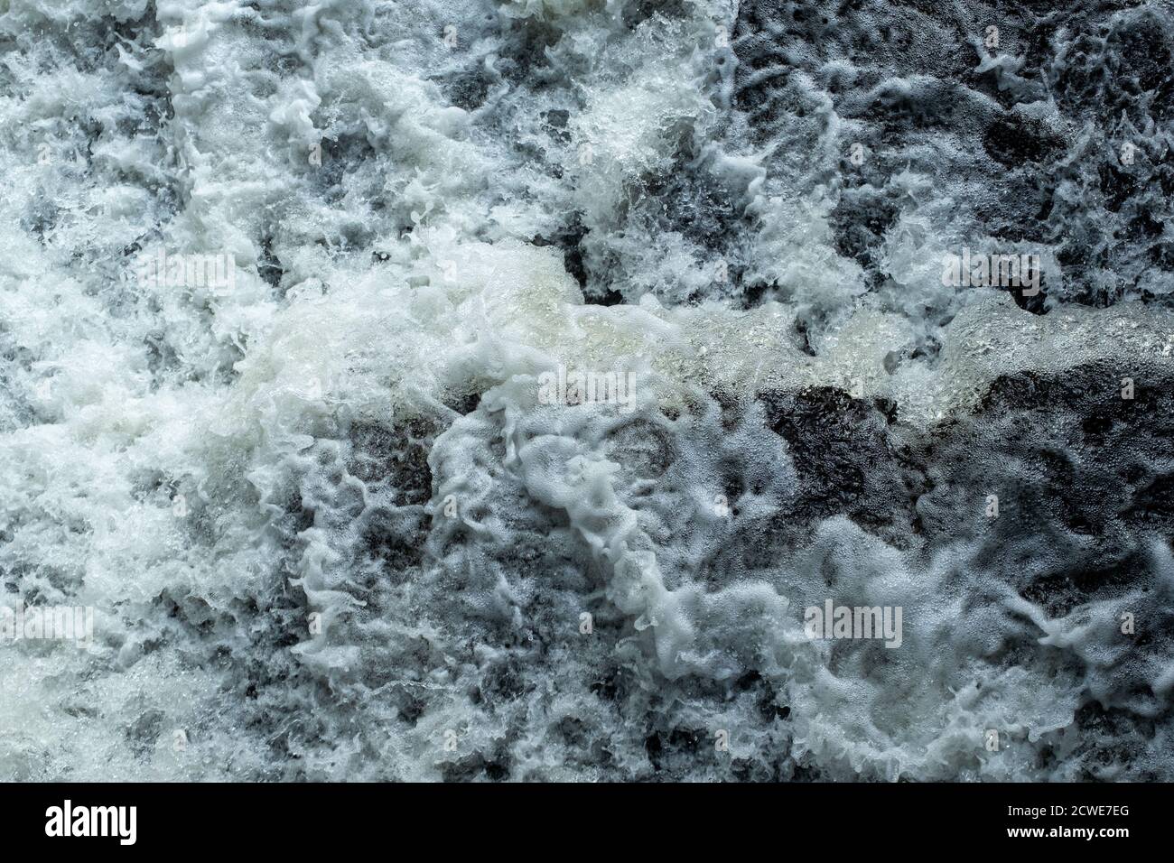Flusswasser, das durch eine Öffnung rauscht, wird von oben als ein Abschnitt fallenden Wildwassers gesehen, der strukturierte Blasen und Bewegungen zeigt. Stockfoto