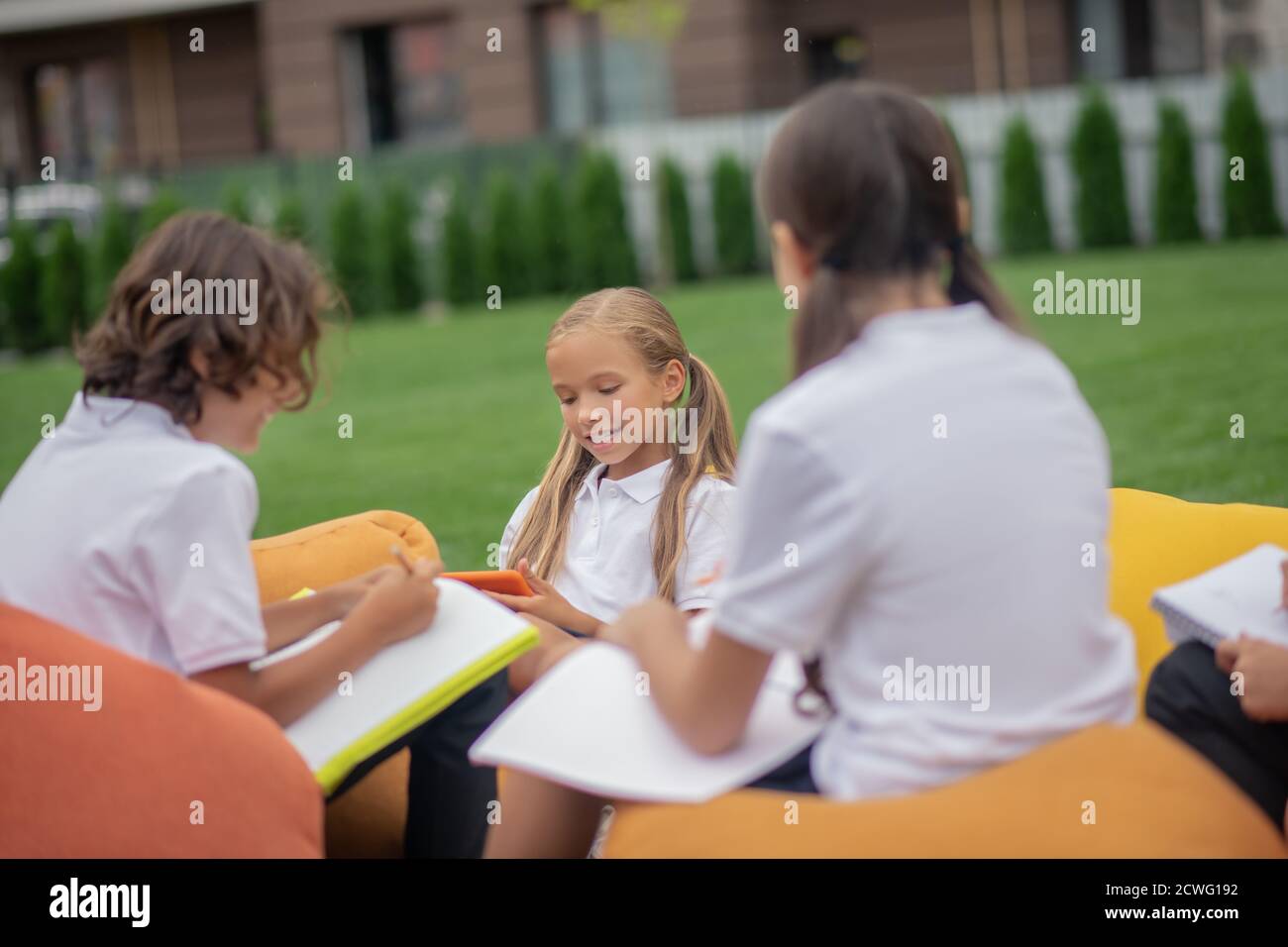 Kinder in weißen Hemden sitzen und studieren gemeinsam draußen Stockfoto