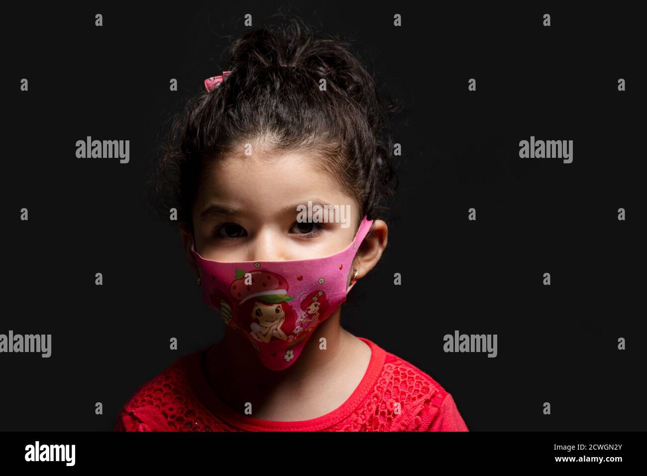 Kleines Mädchen trug Maske zum Schutz vor epidemischen Coronavirus vor dunklem Hintergrund, Coronavirus Ausbruch und Luftverschmutzung Konzept Stockfoto