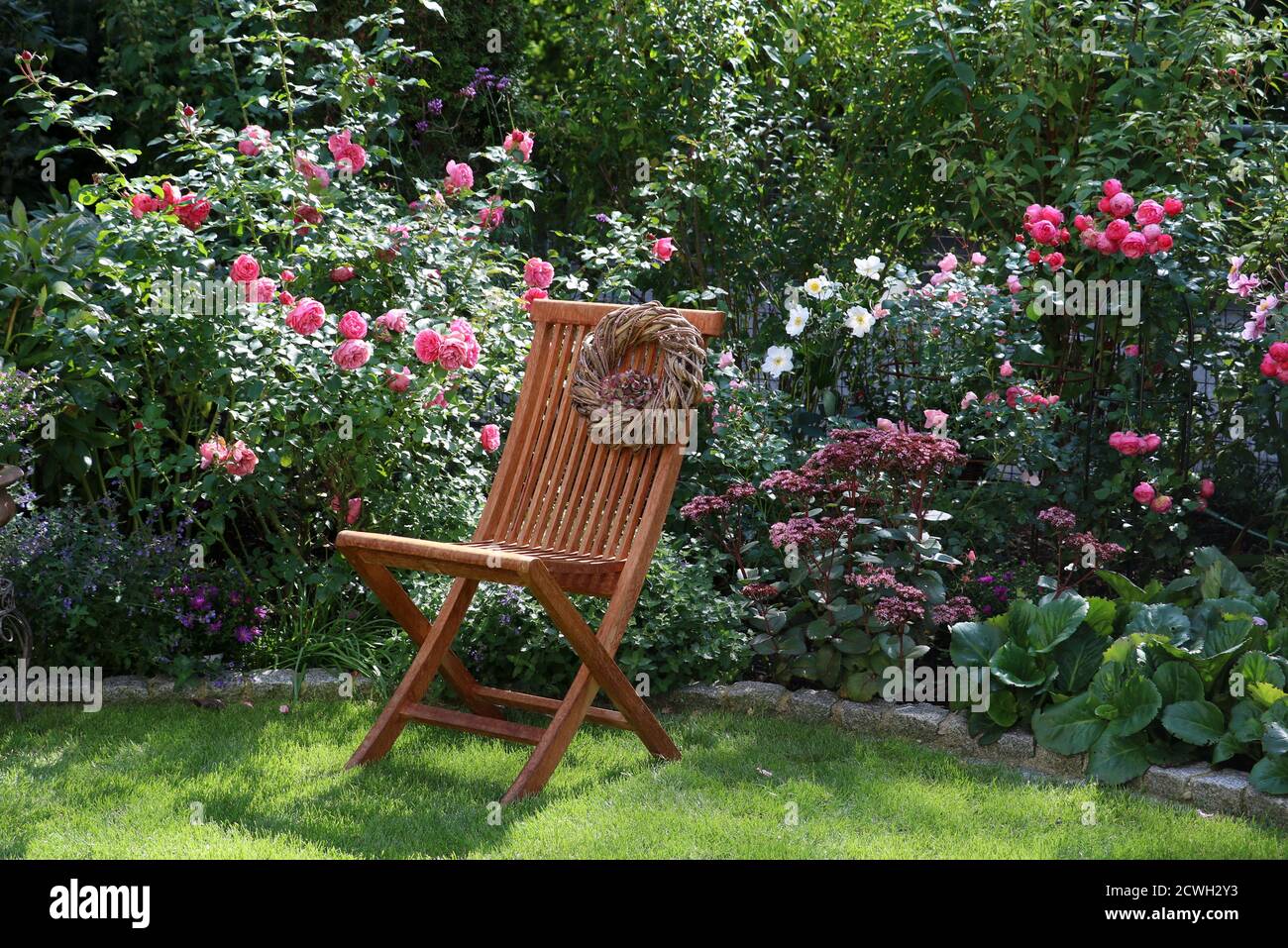 Sommergarten mit rosa Blumen und Holzgartenstuhl Stockfoto