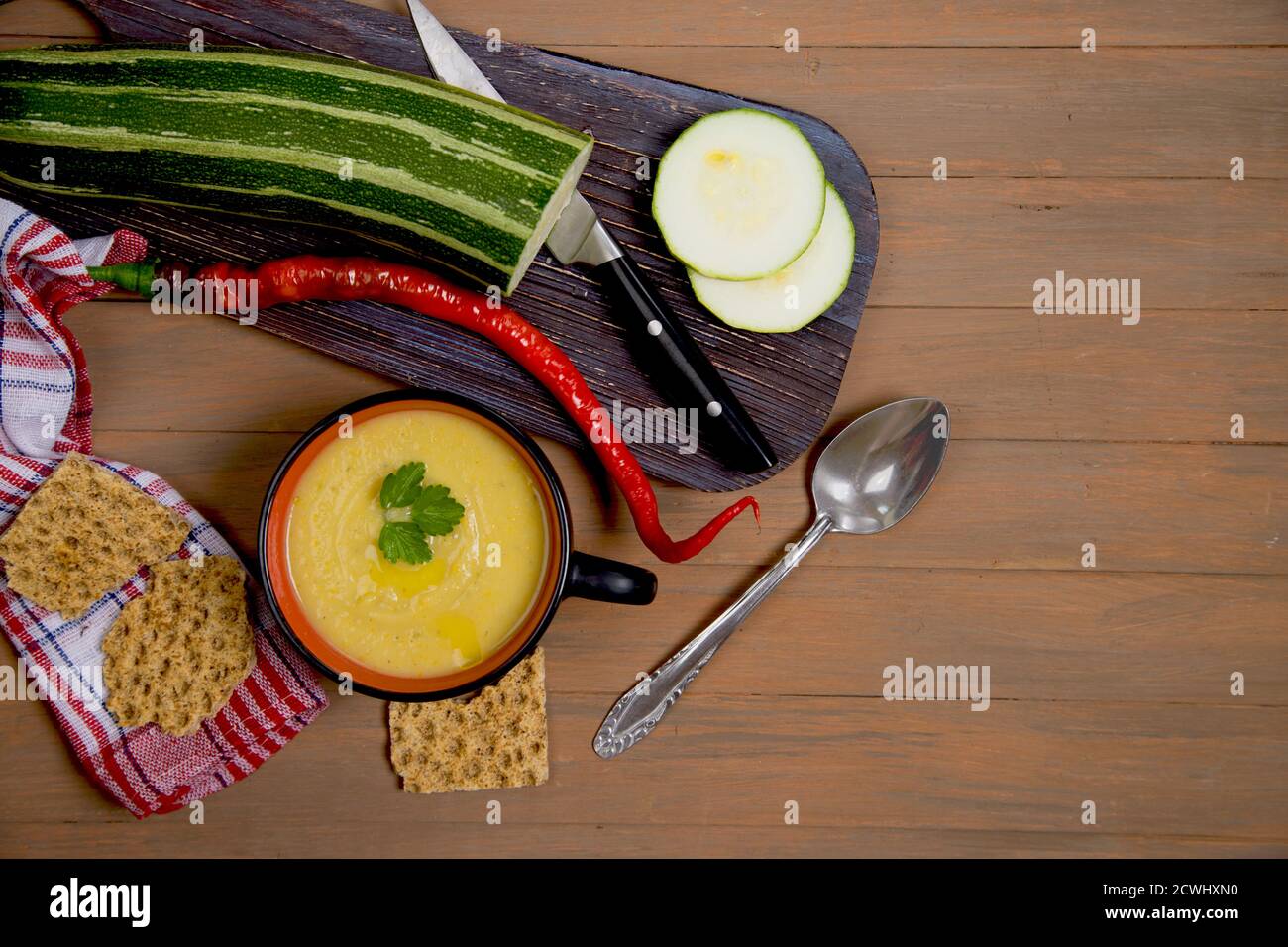 Herbstliche Suppen-pürierte Zucchini und Kürbis auf braunem Holzgrund, Zucchini in Scheiben geschnitten auf einem Holzbrett, Getreidecracker auf roter Serviette, roter P Stockfoto