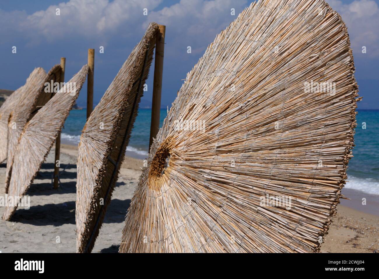 Reihen von Regenschirmen aus Stroh. Wicker Dach Sonnenschirm entfernt und lehnte sich gegen ihre Basis, stehen in einer Reihe auf einem Sandstrand mit azurblauem Meer wat Stockfoto