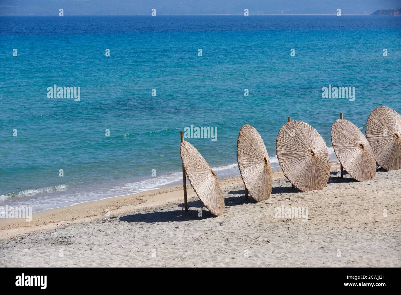 Stroh-Sonnenschirme aus der Sonne sind für den Abschluss der Strandsaison vorbereitet. Hüte Sonnenschirme stehen in einer Reihe an einem Sandstrand mit azurblaues Meer wat Stockfoto