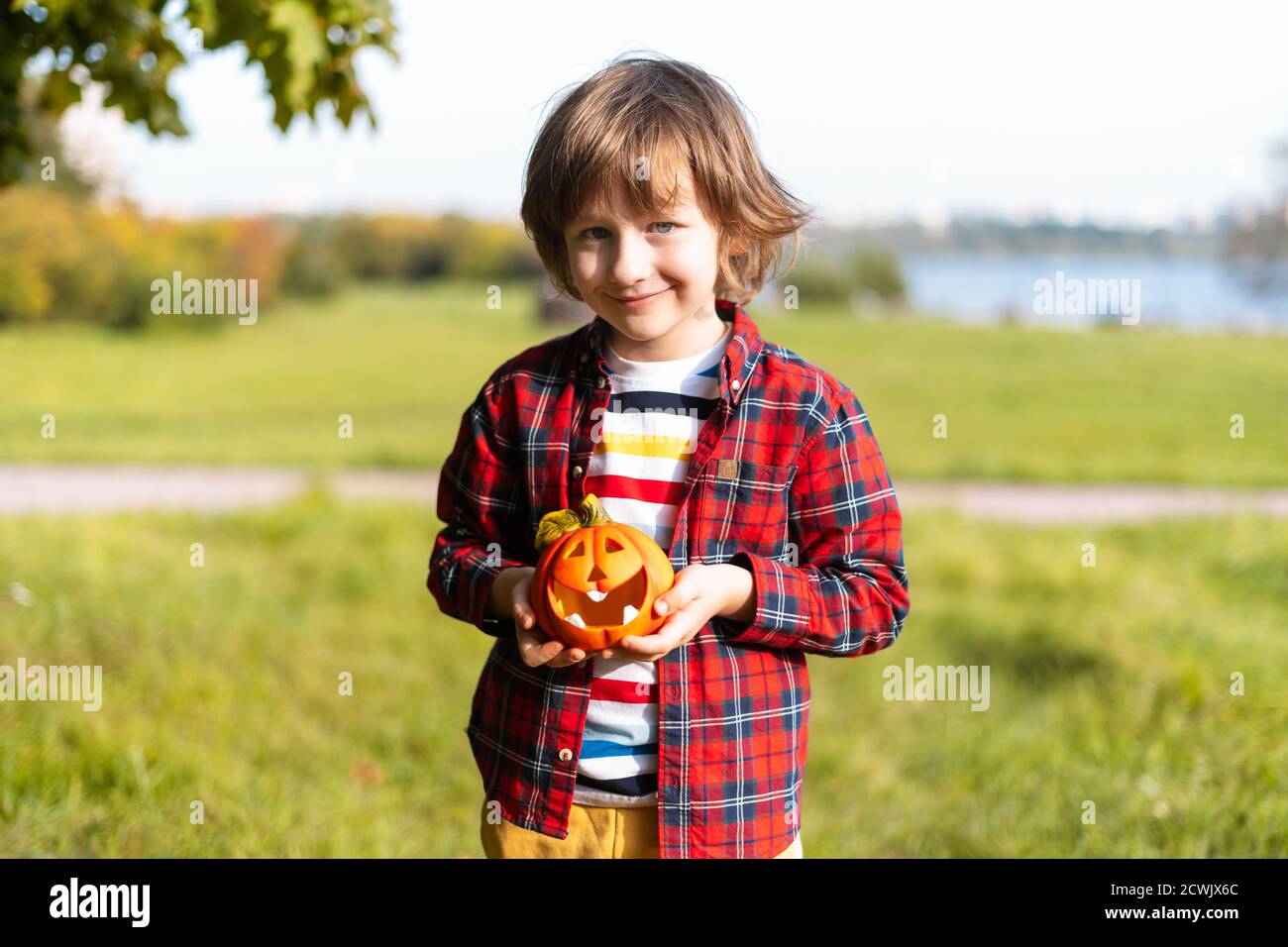 Niedlicher Junge spielen mit Kürbis im Herbstpark an Halloween. Kinder Trick or Treat. Spaß im Herbst. Verkleidetes Kind Stockfoto