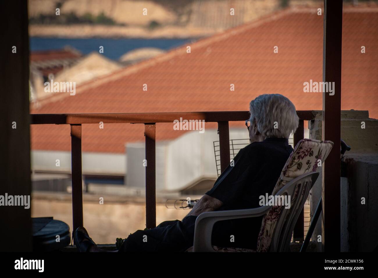Ältere Frau, die vom eigenen Balkon aus das Stadtleben von Chania, Kreta, beobachtet. Stockfoto