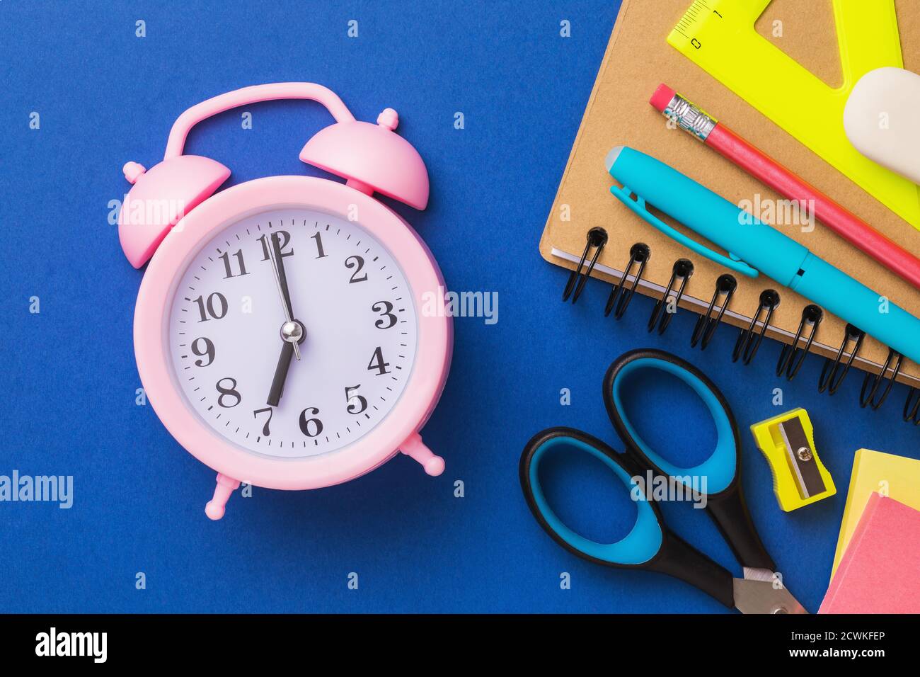 Wecker und Schulbedarf auf blauem Hintergrund, Draufsicht. Konzept zum Thema Schulvorbereitung. Stockfoto