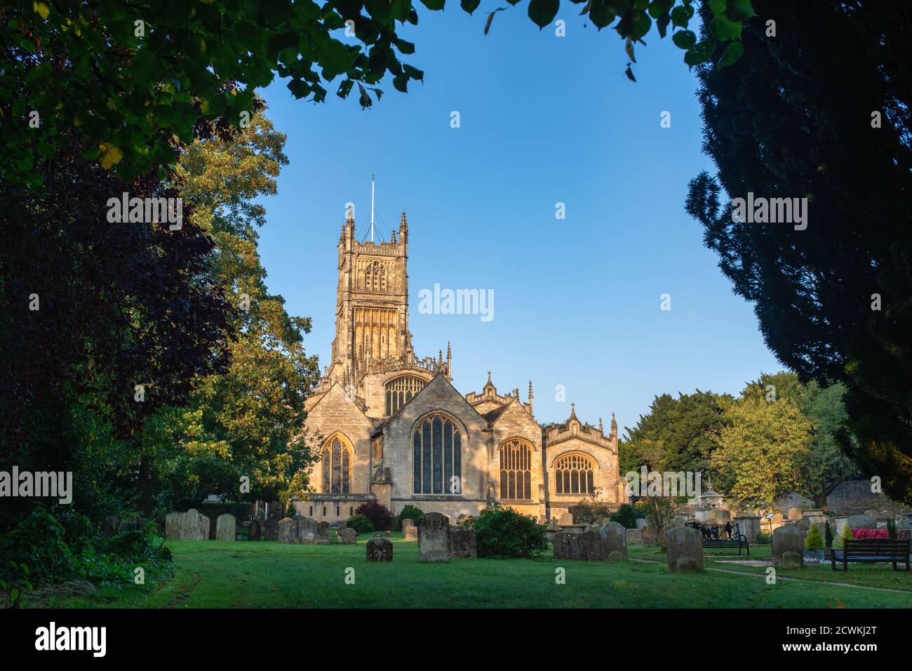 Die Kirche des heiligen Johannes des Täufers aus dem Garten der Erinnerung bei Sonnenaufgang im Herbst. Cirencester, Cotswolds, Gloucestershire, England Stockfoto