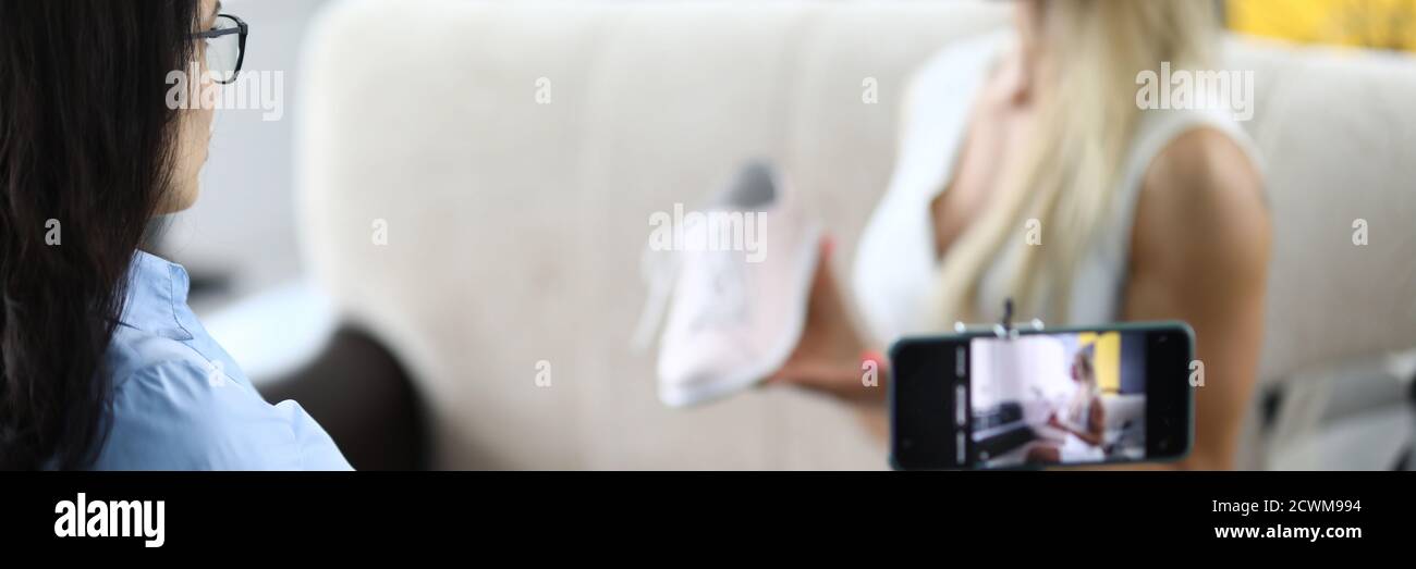 Frau demonstriert Sportschuhe und schreibt Produktbewertung auf ihrem Smartphone Stockfoto