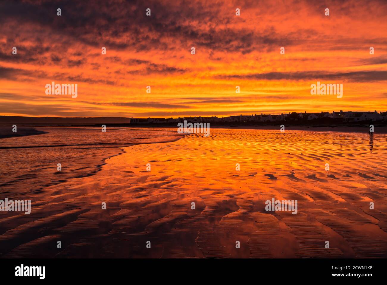 Feurig rötlich/orange Morgenröte Beleuchtung auf Wolken und Sand am Strand von Paternoster in Südafrika. Stockfoto